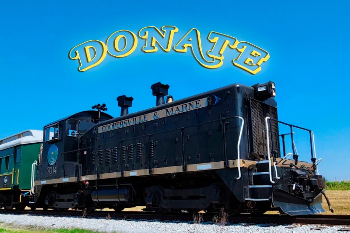Black locomotive on tracks under clear blue sky with 'DONATE' text above.