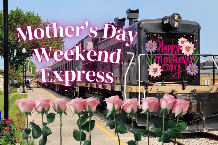 Train with 'Happy Mother's Day' sign, pink roses in front, buildings and blue sky in background.